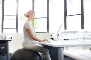 De-stress at your desk - ways to look after your health and wellbeing at work. Woman on swiss ball at her desk.