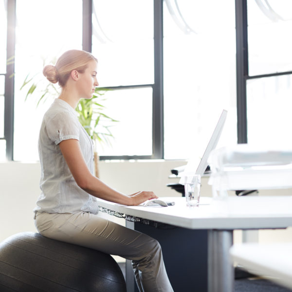 De-stress at your desk - ways to look after your health and wellbeing at work. Woman on swiss ball at her desk.