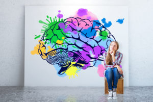 The mind and it's potential - creative thinking concept - Young woman sitting in concrete room with colorful brain sketch on banner.