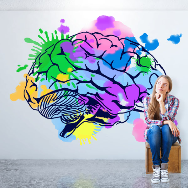 The mind and it's potential - creative thinking concept - Young woman sitting in concrete room with colorful brain sketch on banner.