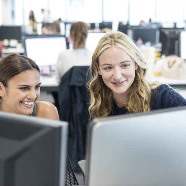 Two women working in office looking at computer, smiling. Demonstrating building a great company culture.