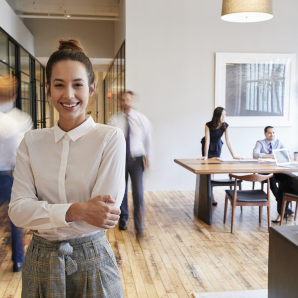 Portrait of young woman in a busy modern workplace - representing how to be happy at work concept