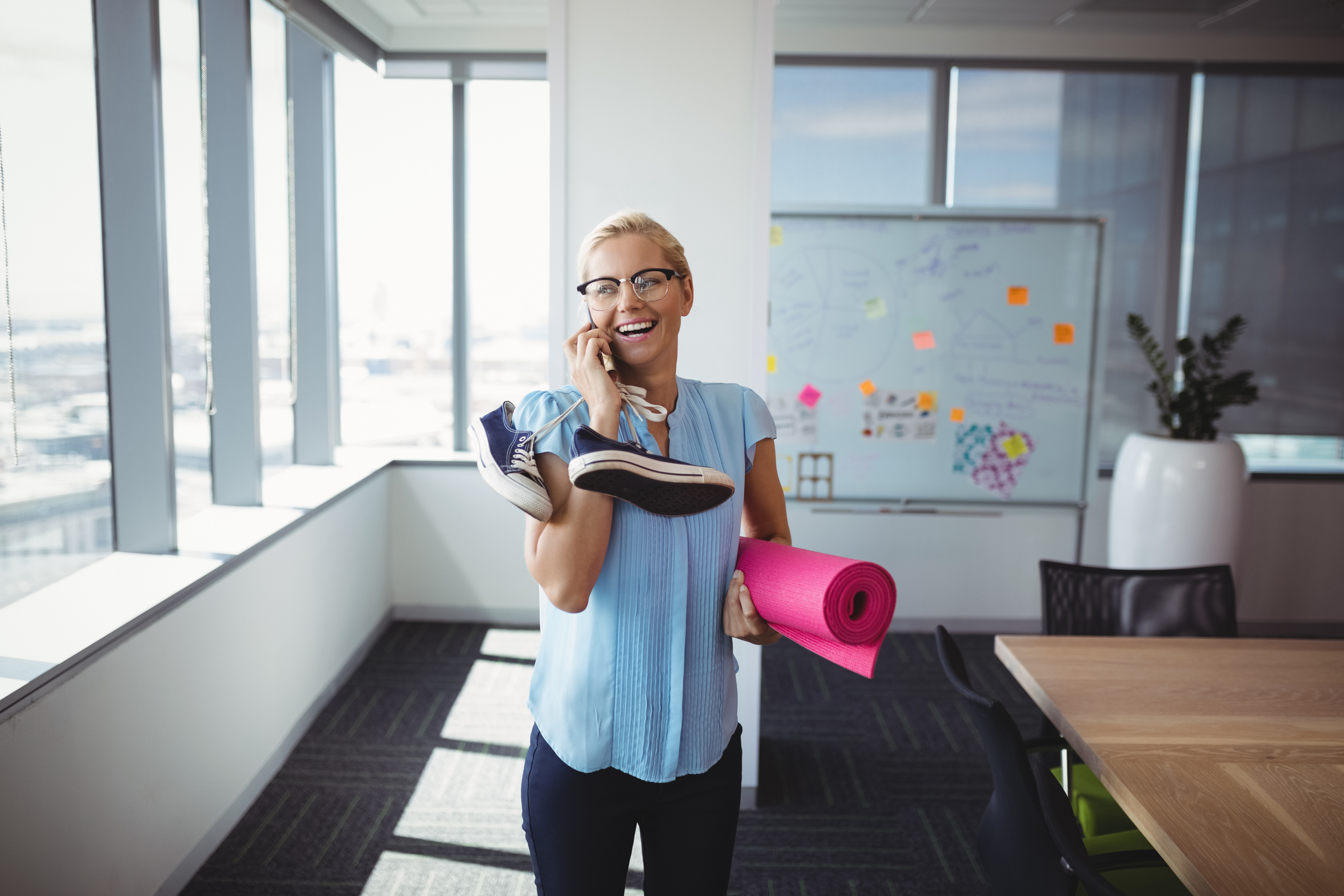 Corporate health and wellbeing - Smiling executive talking on mobile phone while holding exercise mat and shoes